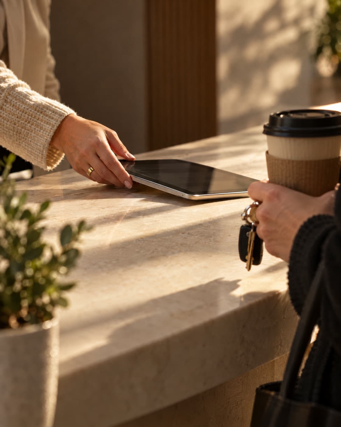 A front desk coordinator sliding a check-in tablet across the counter to an arriving client